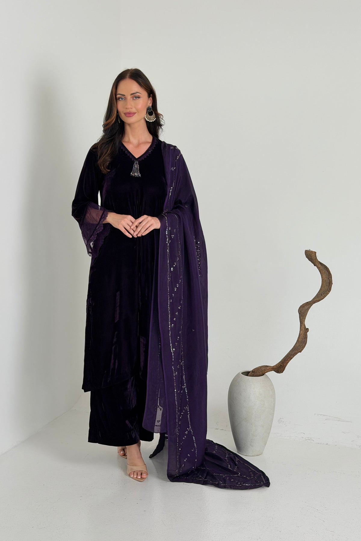 A woman models a dark purple velvet traditional outfit with a matching sheer embroidered dupatta.